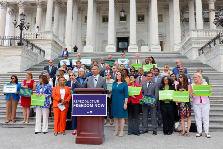 Leader Jeffries speaks behind a podium that reads, Reproductive Freedom Now in front of many Members of Congress.